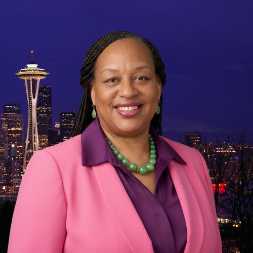 Jeanine Burnley, Executive Director of Agape Love of Renton, smiling in front of the Seattle skyline at night